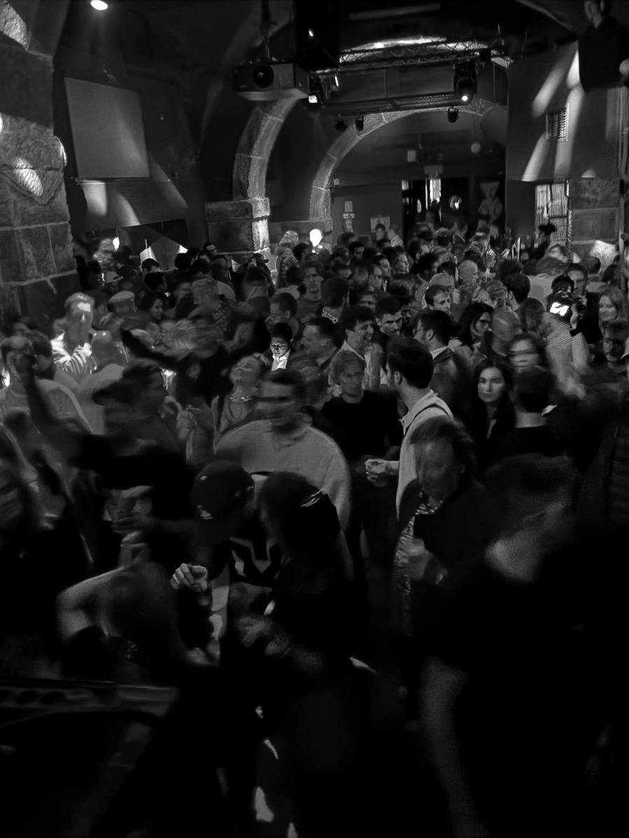 Crowded dance floor in a historic stone venue lit by purple and blue lights